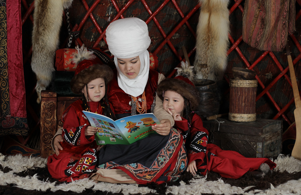 Mother and her daughters in traditional clothes read books © Taalim-Forum
